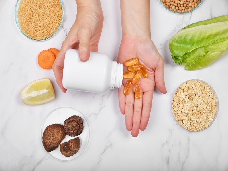 Manos sirviendo cápsulas de suplementos junto a alimentos naturales como vitaminas para el cerebro.